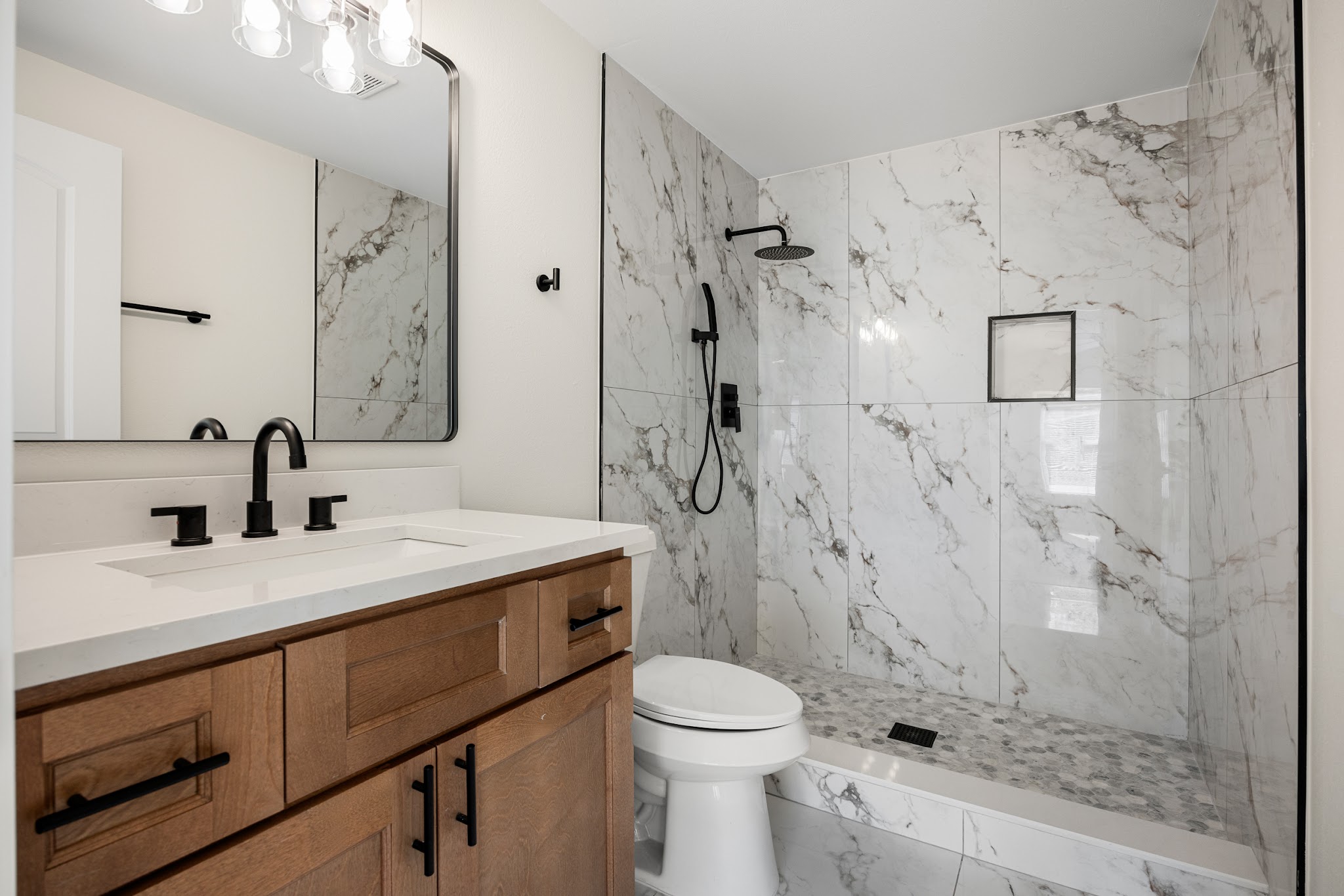 Marble tile shower and wood vanity in a completed bathroom remodel